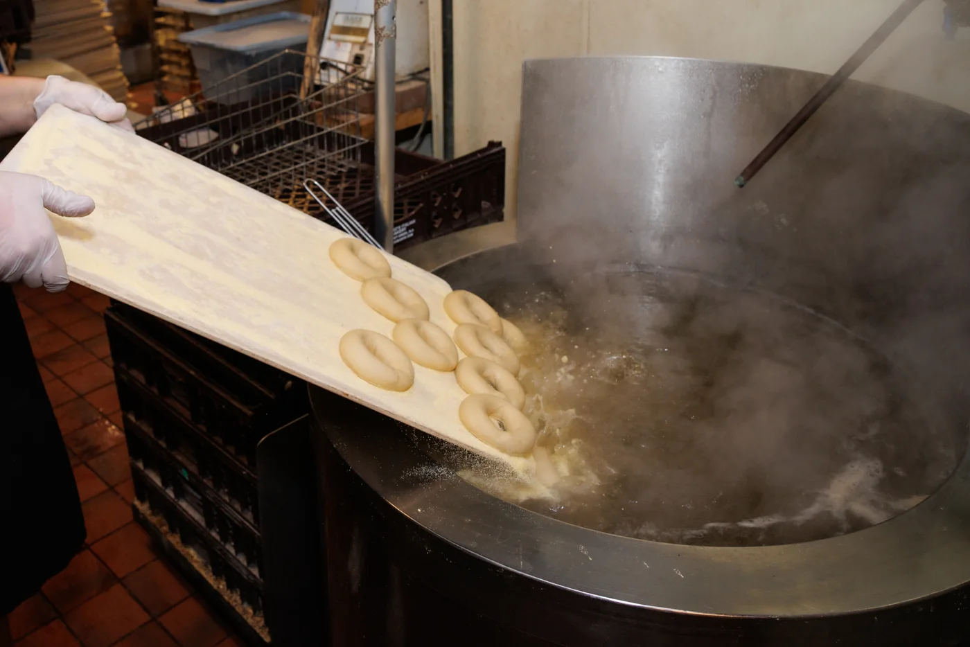 Bagels sliding from a wooden board into the steaming kettle