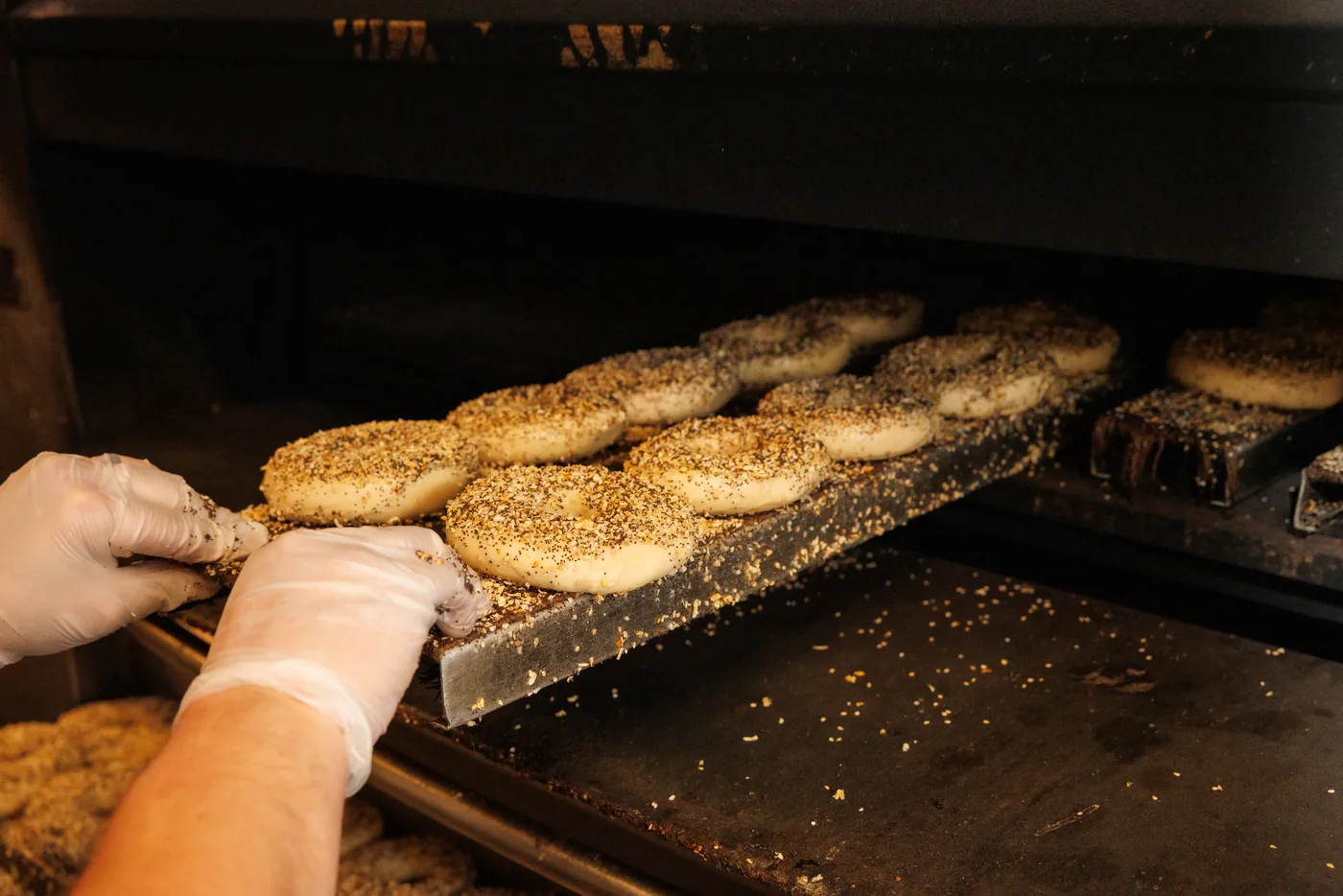 A baker loading boards of seeded bagels into the oven
